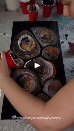 a woman is painting some brown and white pots with red cups on the table next to her