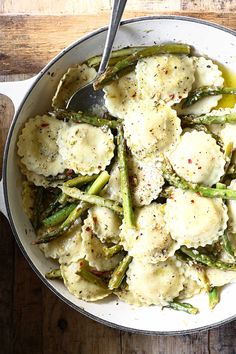 a bowl filled with ravioli and asparagus on top of a wooden table