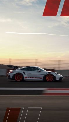 a white sports car driving down a race track at sunset or sunrise with the sun setting behind it