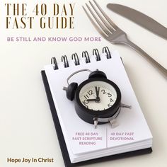 an alarm clock sitting on top of a notepad next to a fork and knife