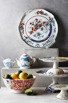 an assortment of plates and bowls with fruit in them sitting on a counter top next to a wall