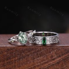 two wedding rings with green and white stones on top of a wooden table in front of a black background