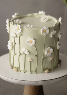 a green cake with white flowers on it sitting on top of a wooden stand next to a potted plant