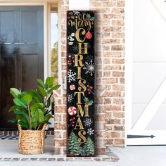 a wooden christmas sign sitting on the side of a brick building next to a potted plant