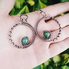 a hand holding a pair of silver hoop earrings with green stones on it's sides