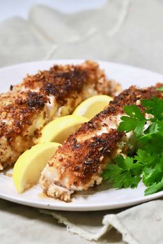 two pieces of chicken on a plate with parsley garnish and lemon wedges