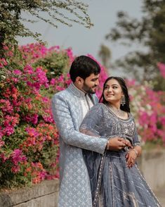 a man and woman standing next to each other in front of flowers