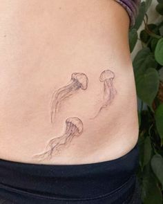 a woman's stomach with two jellyfish tattoo on her lower back and side