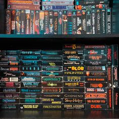 several books are stacked on top of each other in front of a book shelf filled with dvds