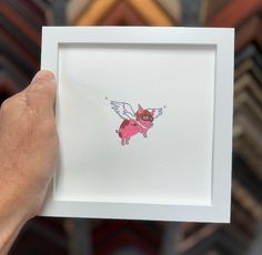 a hand holding up a small pink pig with wings