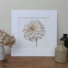 a white flower sitting on top of a table next to a vase filled with flowers