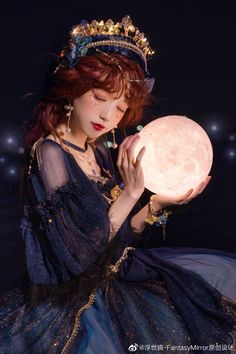 a woman in a blue dress holding a light up moon ball with stars on the background