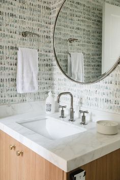 a bathroom sink under a round mirror next to a wooden cabinet with two towels hanging on it