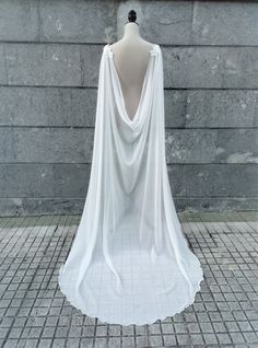 a mannequin wearing a white draped dress on a brick floor next to a wall