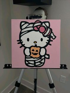 a hello kitty holding a pumpkin in her arms on a pink background with black and white stripes