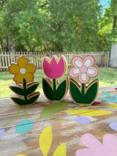 three wooden flowers sitting on top of a table in front of a fence and trees