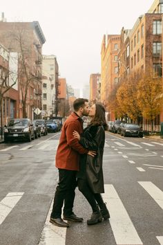 a man and woman kissing in the middle of an empty street with cars parked on both sides