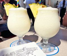 two glasses filled with white liquid and topped with pineapple slices, sitting on a table