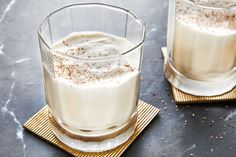 two glasses filled with liquid sitting on top of a table next to gold coasters