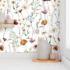 a white vase sitting on top of a counter next to a wallpaper covered in flowers