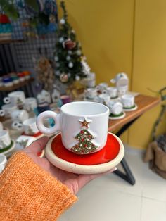 a hand holding a coffee cup with a christmas tree on the top and saucer