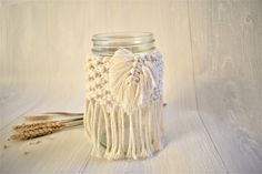 a white crocheted mason jar with tassels next to it on a wooden table