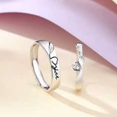 two silver rings with hearts on them sitting next to each other, against a pastel background