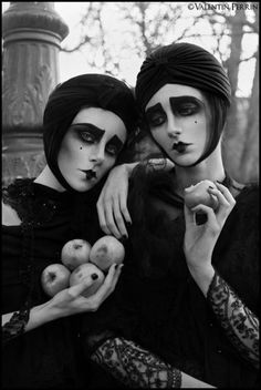 two women dressed in black are holding apples and posing for the camera with their faces painted