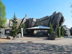 a large rock formation in front of a building with trees and people walking around it