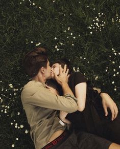 two people laying on the ground kissing each other with flowers in the backgroud