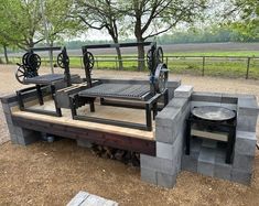 an outdoor grill made out of cinder blocks and wood with wheels on the top, sitting in front of a tree