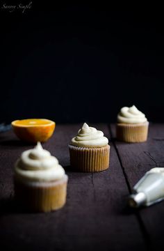 three cupcakes with icing and an orange slice on the table next to them