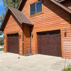 two brown garage doors are open in front of a house with wood siding and shingles