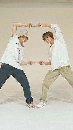 two young men standing next to each other in front of a white wall holding hands