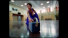 a woman sitting on top of a blue suitcase in a room with wooden flooring