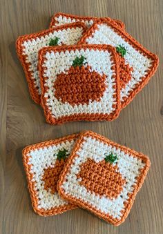 four crocheted coasters are sitting on a wooden table with orange and white designs