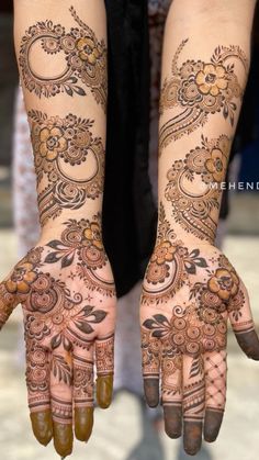 two hands with henna tattoos on them, one is showing the intricate design and the other has flowers