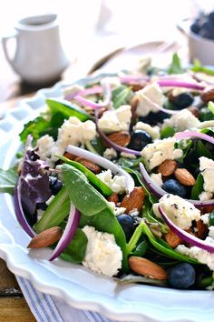 a salad with blueberries, spinach and feta cheese on it is sitting on a white plate