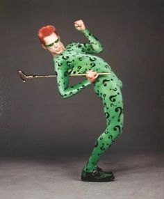 a man dressed in green and black holding a cane with question marks on it's body