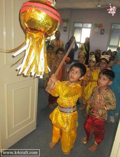 young children dressed in yellow and orange are standing near an open door while holding onto a large golden object