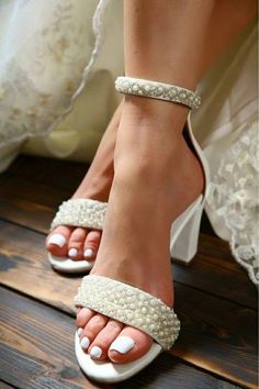 a woman's feet wearing white shoes with pearls on them