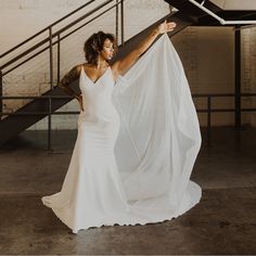 a woman in a white wedding dress is holding up a piece of fabric that has been draped over her head