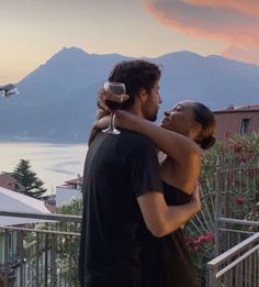 a man and woman standing next to each other on a balcony with mountains in the background