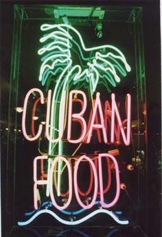 a neon sign that says cuban food in front of a building with palm trees on it