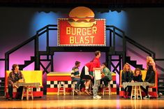 a group of people sitting on top of chairs in front of a burger blast sign