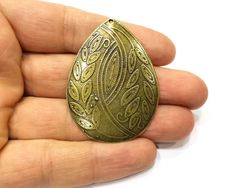 a person is holding an antique brass brooch in their left hand and wearing a ring with intricate designs on it