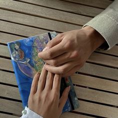 two people holding hands over a book on a wooden bench with the image of mermaids