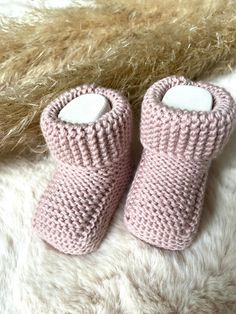 two pink knitted baby booties sitting on top of a white rug