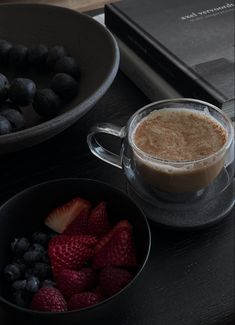 two bowls of berries and a cup of coffee on a table next to a book