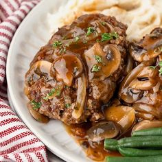 a white plate topped with meat covered in mushroom gravy and mashed potatoes